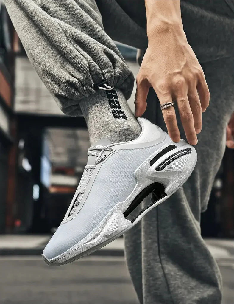 White athletic shoe with black accents worn by a person in gray pants.